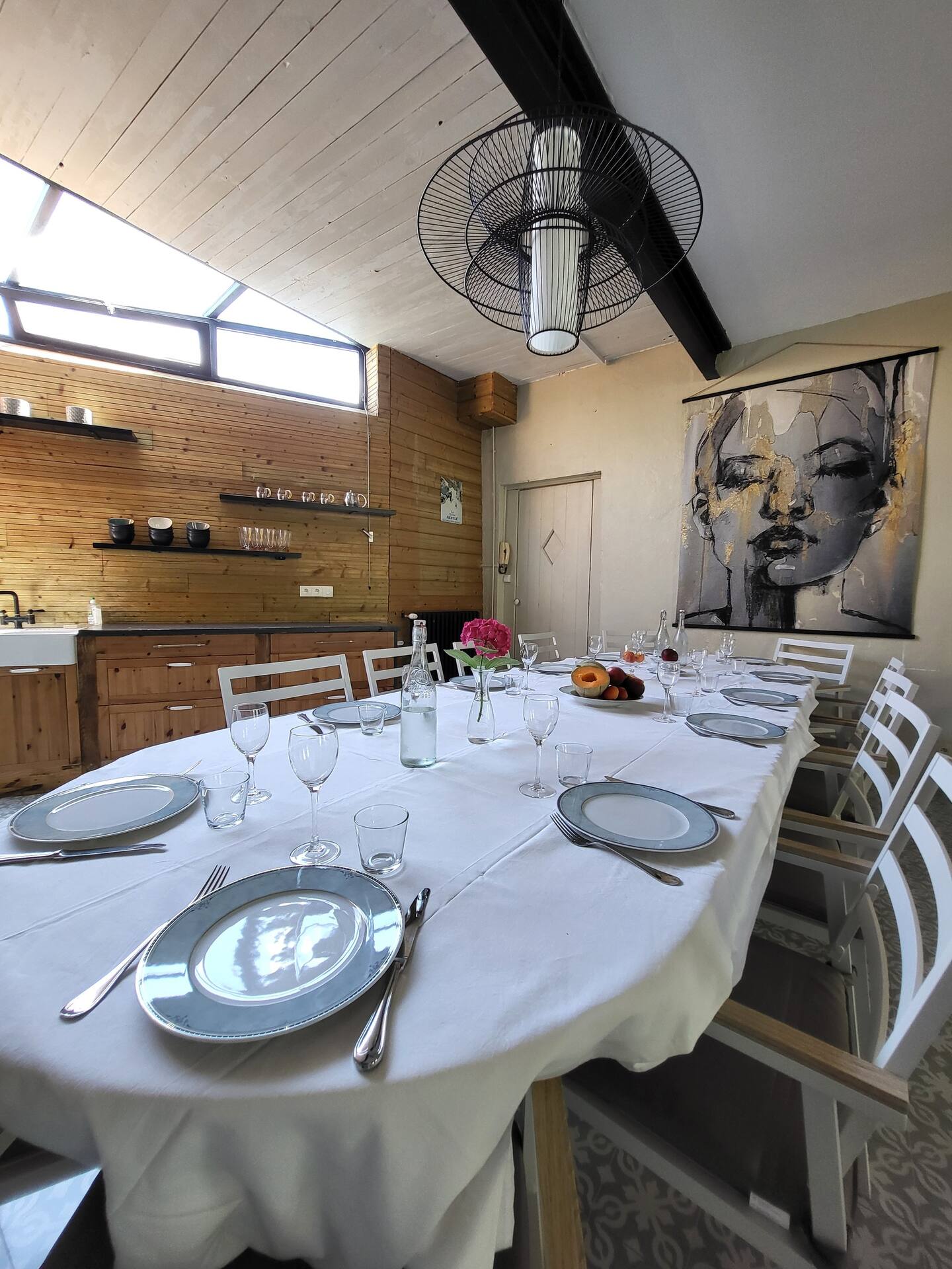 Salle à manger du Gîte L'Intemporelle avec grande table dressée, cuisine ouverte et lumière naturelle.